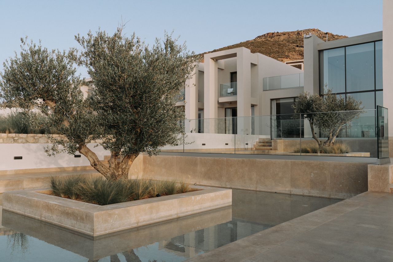 Modern luxury house exterior with glass facade, landscaped garden, and water feature.